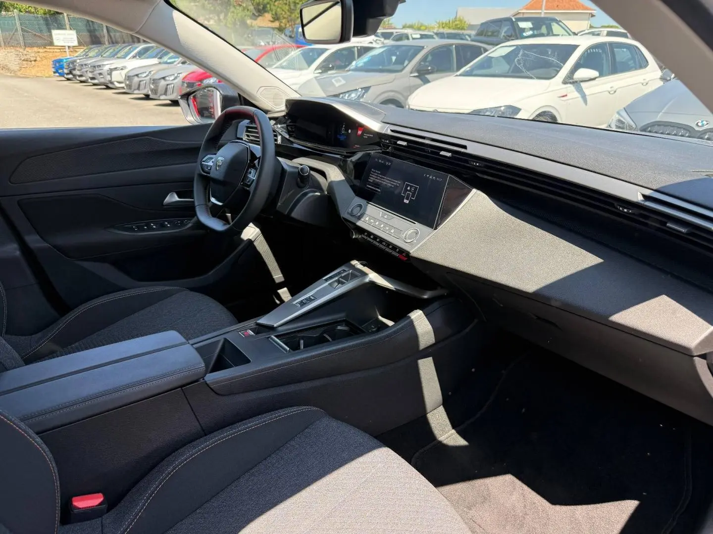 Vue intérieure côté conducteur de la Peugeot e-308 2025, tableau de bord moderne avec écran tactile et sièges tissu gris.