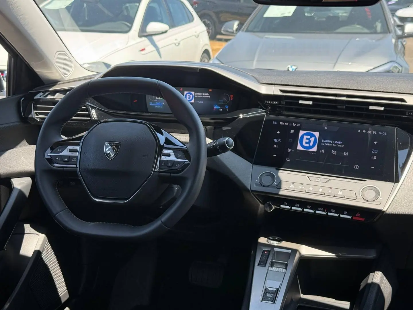 Vue intérieure du poste de conduite de la Peugeot e-308 gris Artense, avec volant multifonction et écran tactile central.