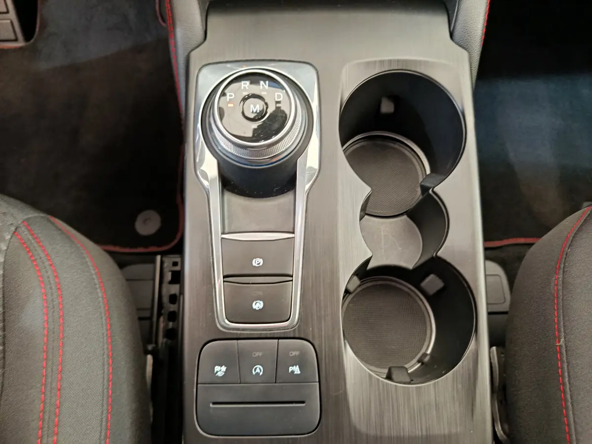 Vue plongeante sur la console centrale noire du Ford Kuga 2024 avec molette de boîte auto et porte-gobelets.