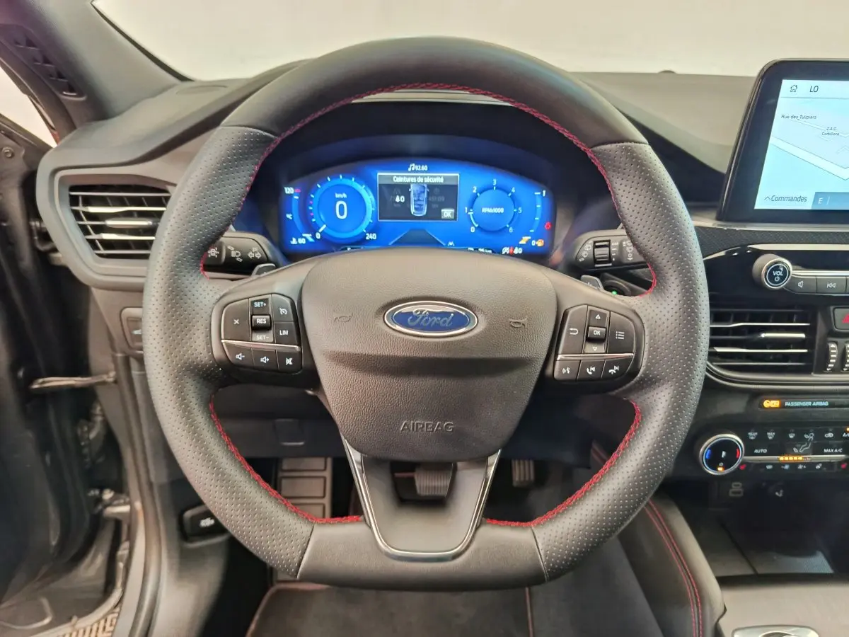 Vue rapprochée du volant noir avec surpiqûres rouges du Ford Kuga 2024, tableau de bord numérique et écran tactile visible.
