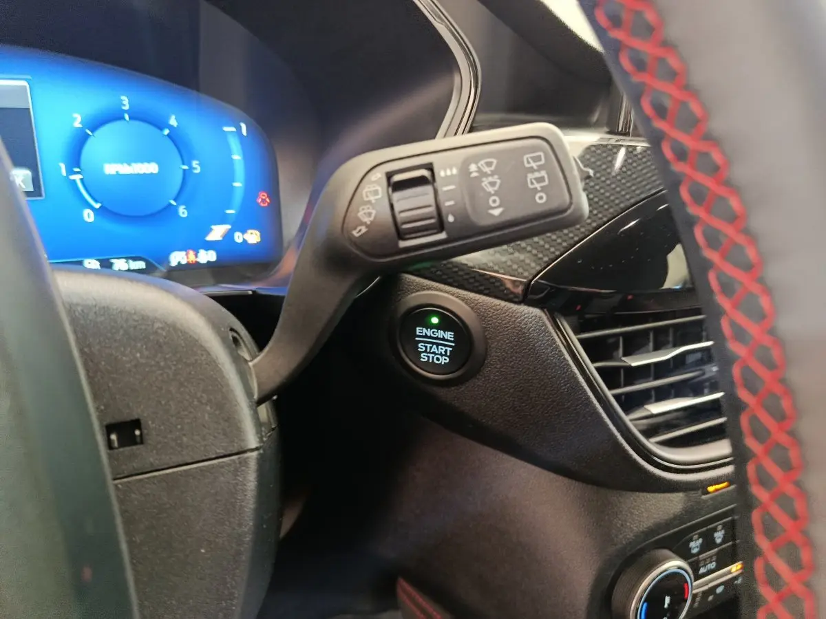 Détail intérieur du tableau de bord du Ford Kuga 2024, bouton démarrage et volant avec surpiqûres rouges visibles.
