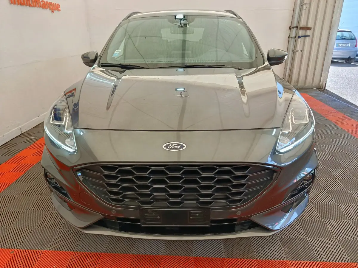 Vue frontale d'une Ford Kuga gris clair 2024 avec calandre hexagonale noire et phares LED allumés.