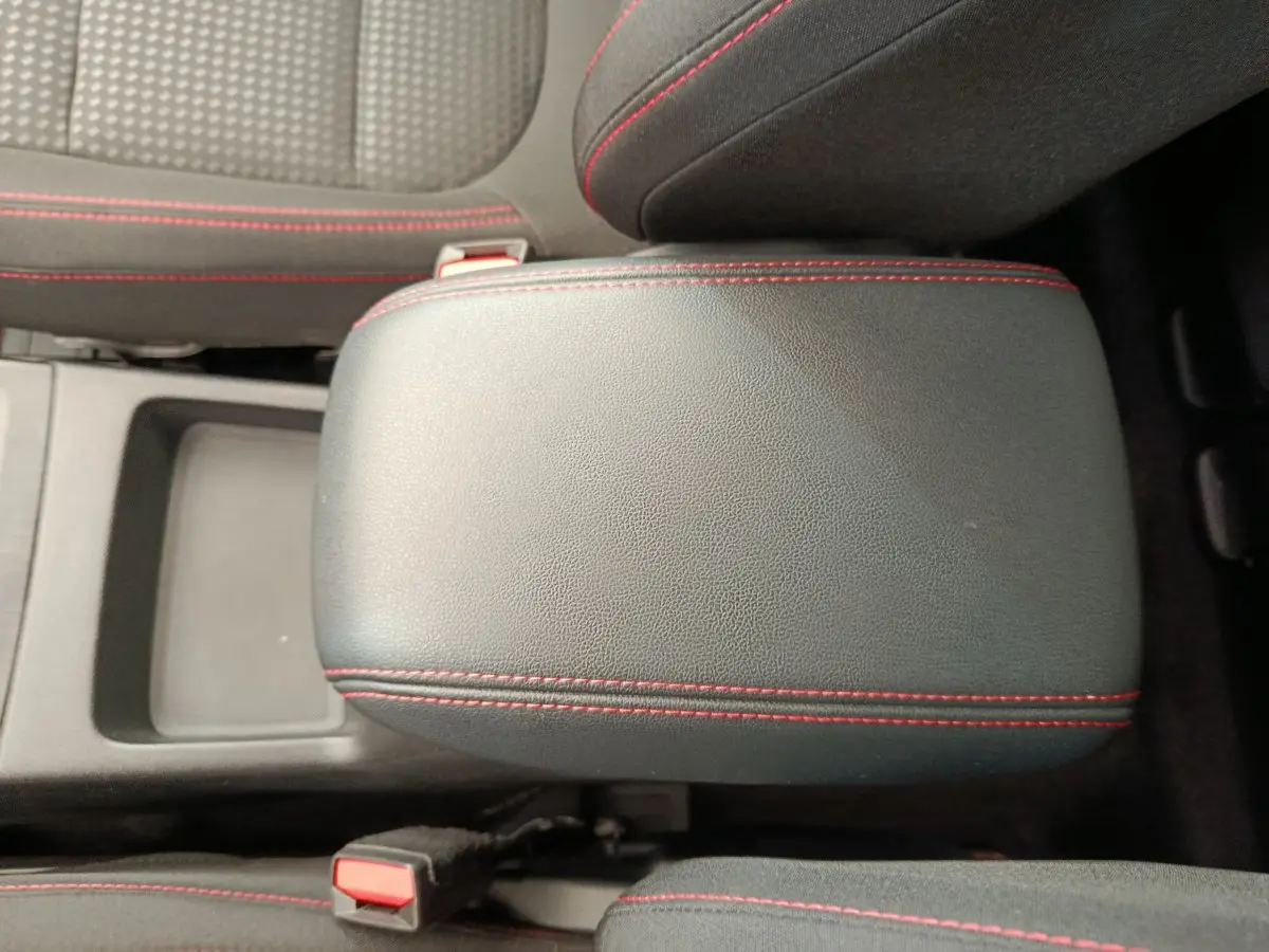 Gros plan sur l'accoudoir central noir avec surpiqûres rouges du Ford Kuga 2024, intérieur tissu gris et noir.