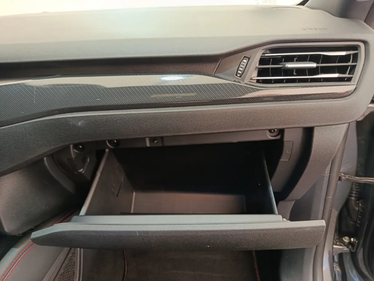 Vue rapprochée de la boîte à gants ouverte côté passager du Ford Kuga 2024 avec tableau de bord gris et insert carbone.