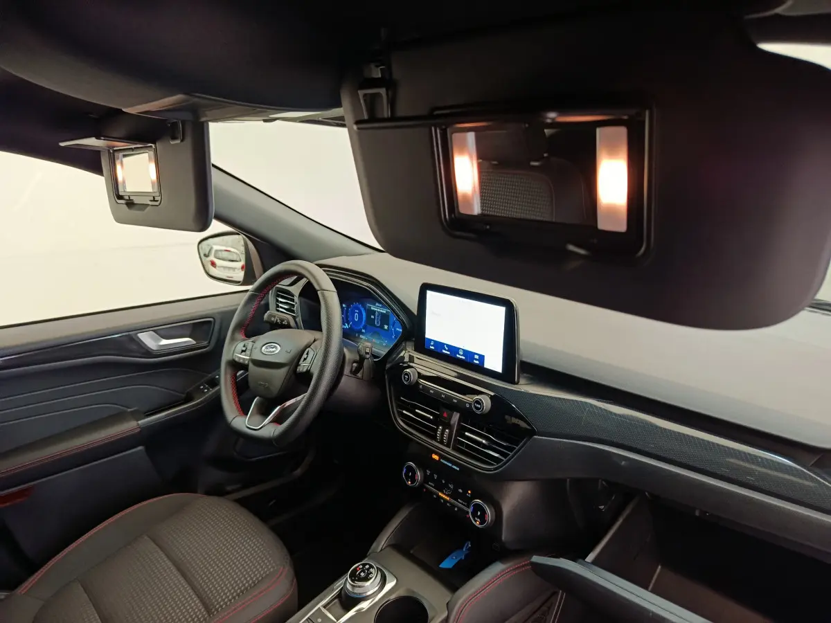 Intérieur du Ford Kuga 2024 en vue côté conducteur, tableau de bord moderne avec écran tactile et volant cuir noir.