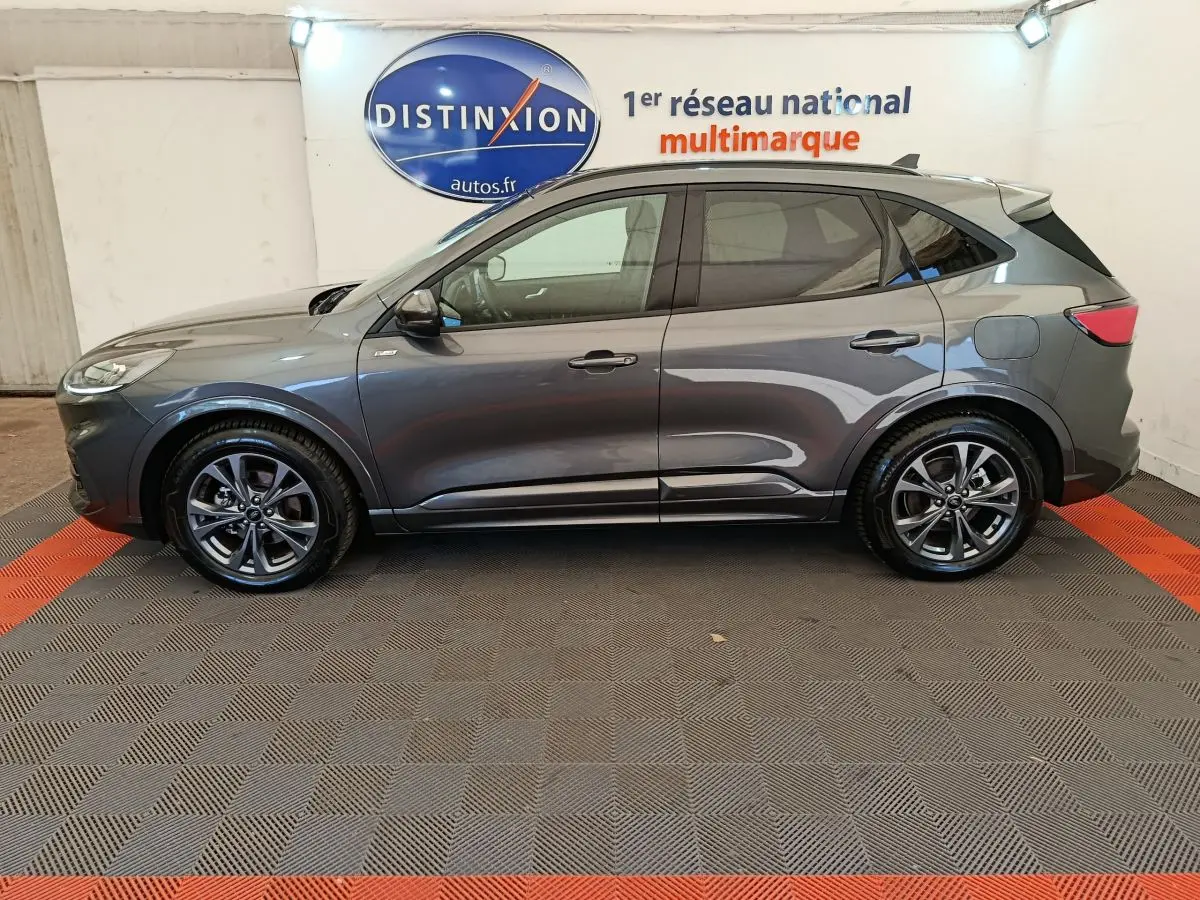 Ford Kuga gris clair vue de profil côté gauche dans un showroom avec logo Distinxion en arrière-plan.