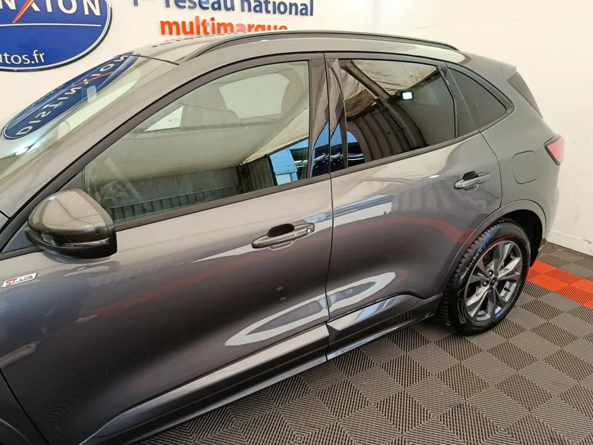 Vue latérale côté gauche d'un Ford Kuga gris clair ST Line avec jantes alliage et vitres teintées.