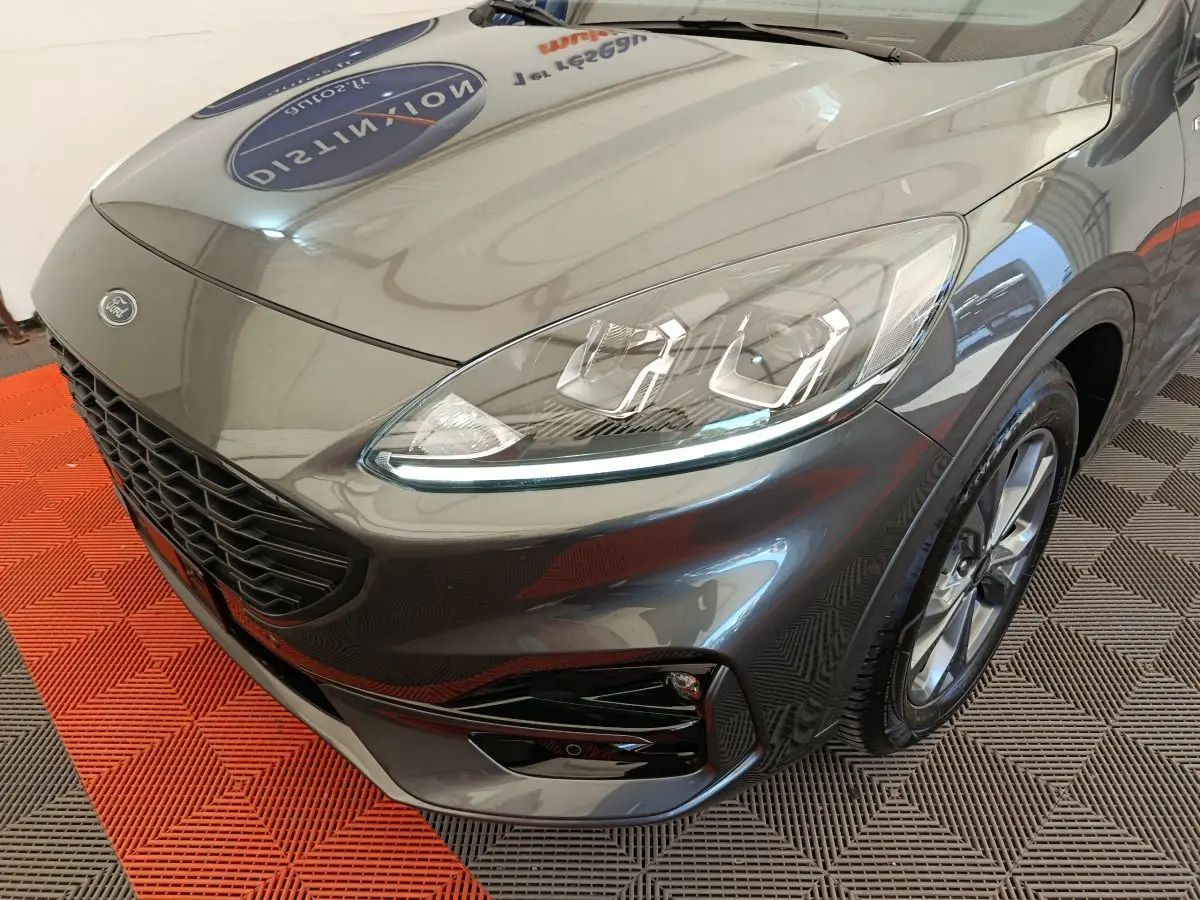 Vue 3/4 avant droit d'un Ford Kuga gris clair mettant en valeur ses phares LED et sa calandre noire sportive.