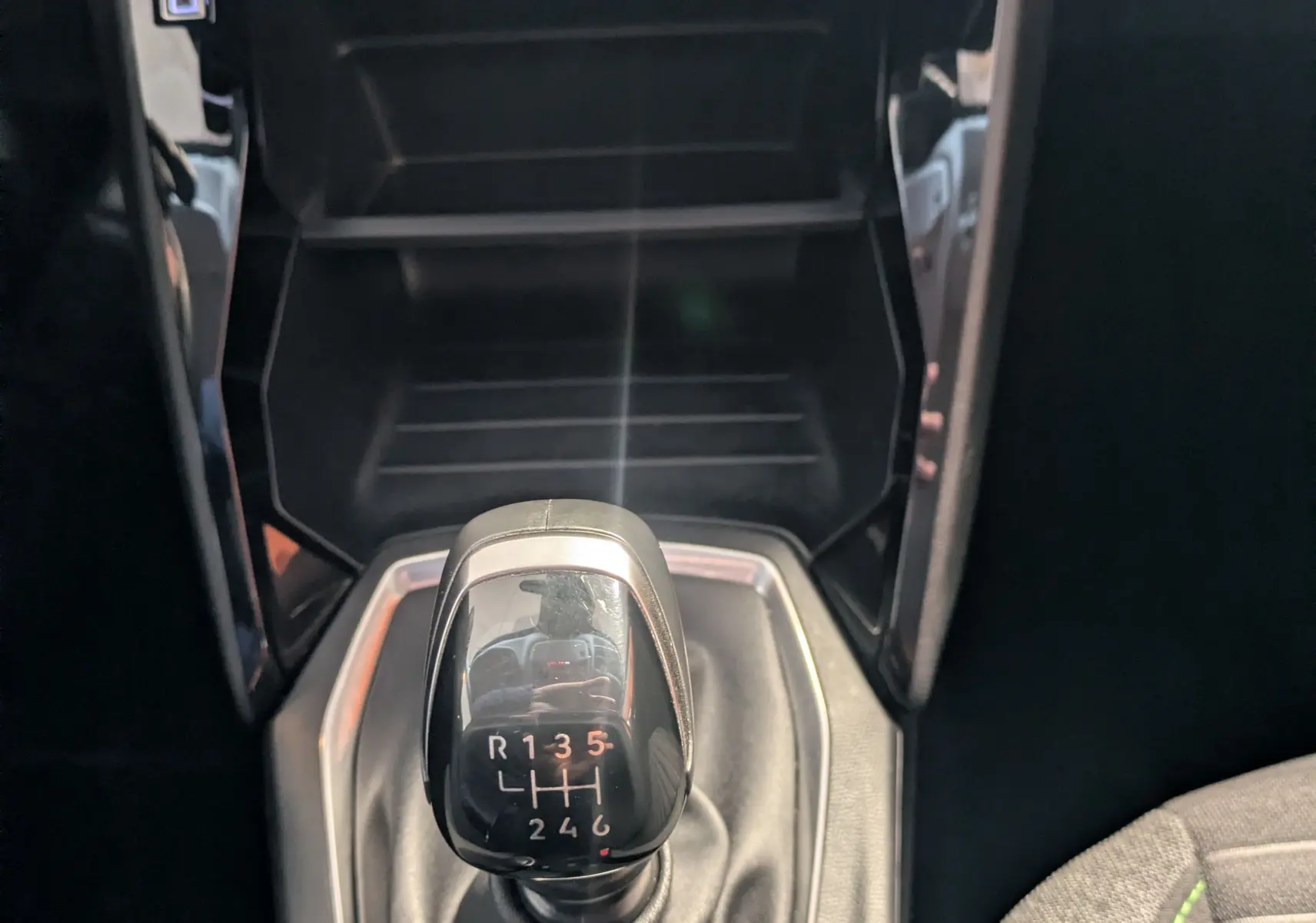 Le levier de vitesses manuel de la Peugeot 208 PureTech 100 noire, vu de dessus avec la console centrale et la sellerie tissu.