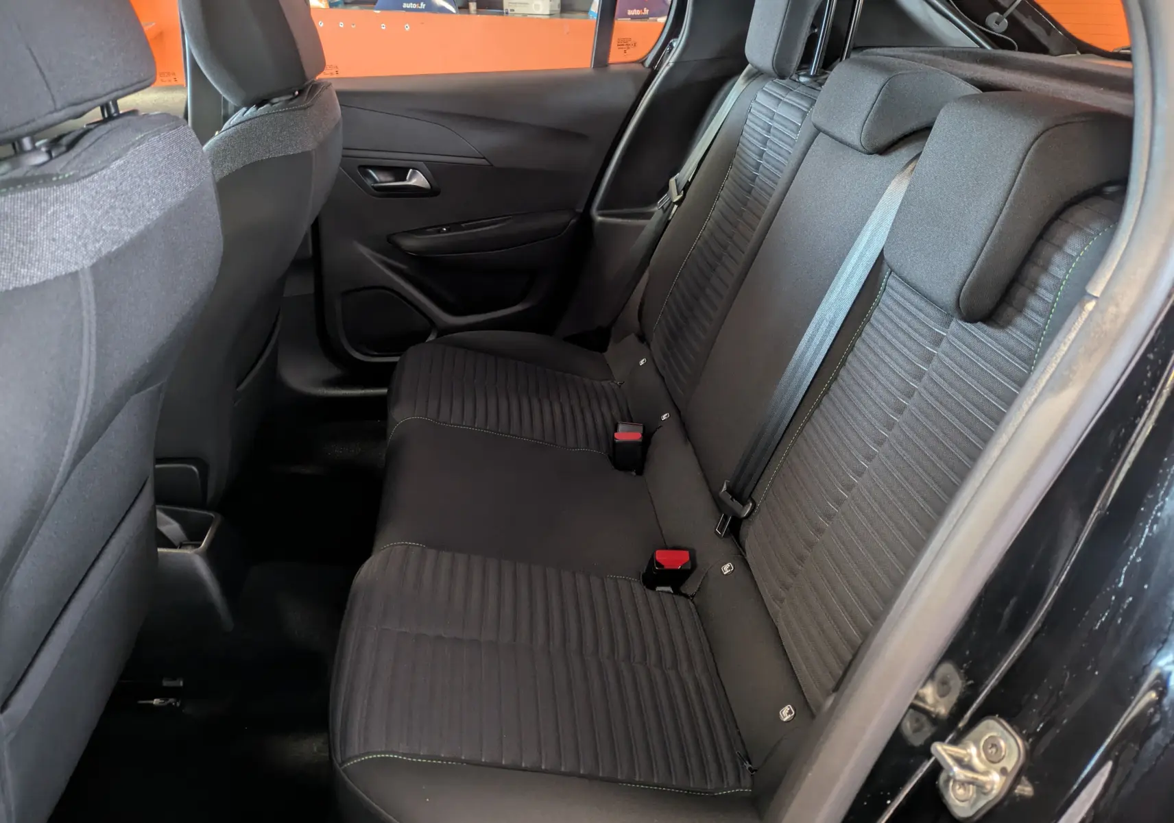 Vue intérieure arrière côté droit du Peugeot 208 noir Perla 2024, sellerie tissu avec surpiqûres vertes et ceintures visibles.