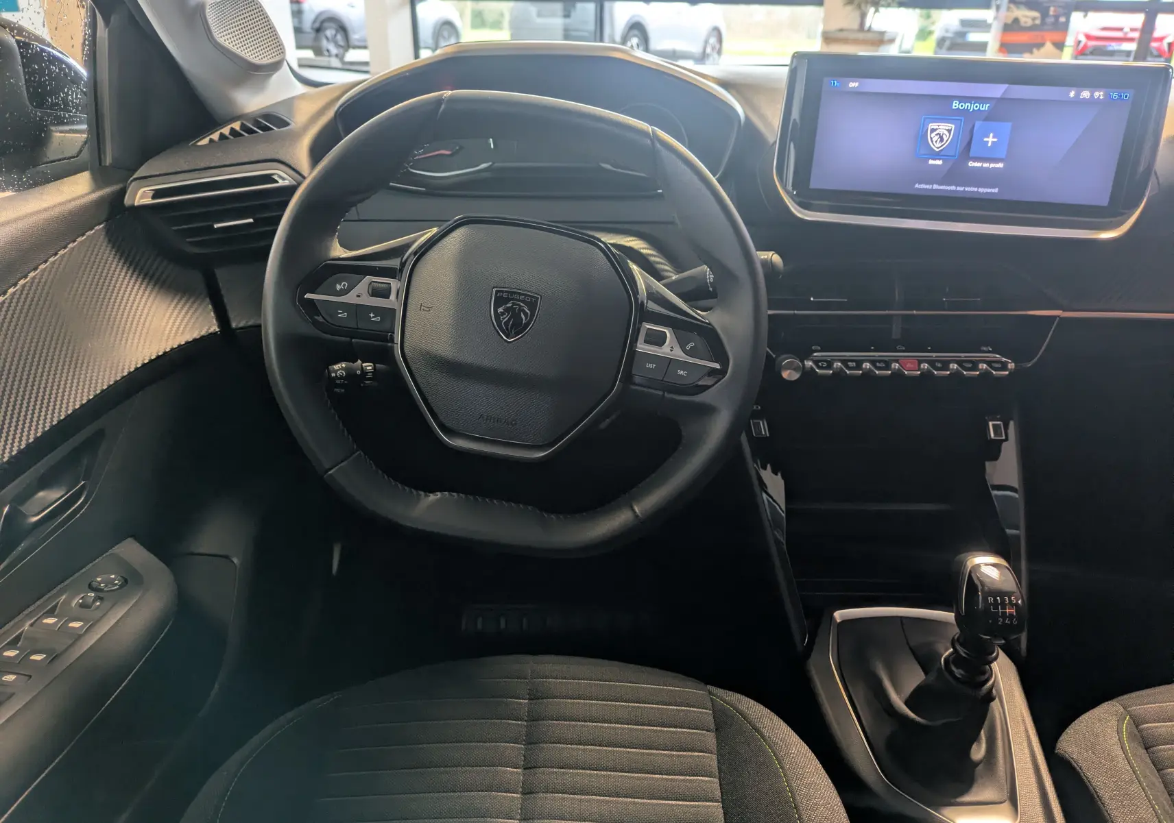 Vue intérieure centrée sur le volant cuir et la console avec écran tactile du Peugeot 208 noir Perla 2024.