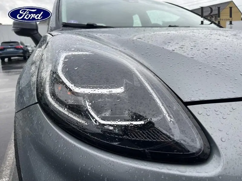 Gros plan sur le phare avant gauche du Ford Puma gris Solar métallisé 2023, avec gouttes de pluie visibles sur la carrosserie.