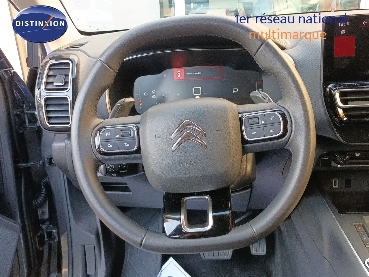 Vue intérieure centrée sur le volant noir du Citroën C5 Aircross 2025 avec tableau de bord numérique et commandes intégrées.