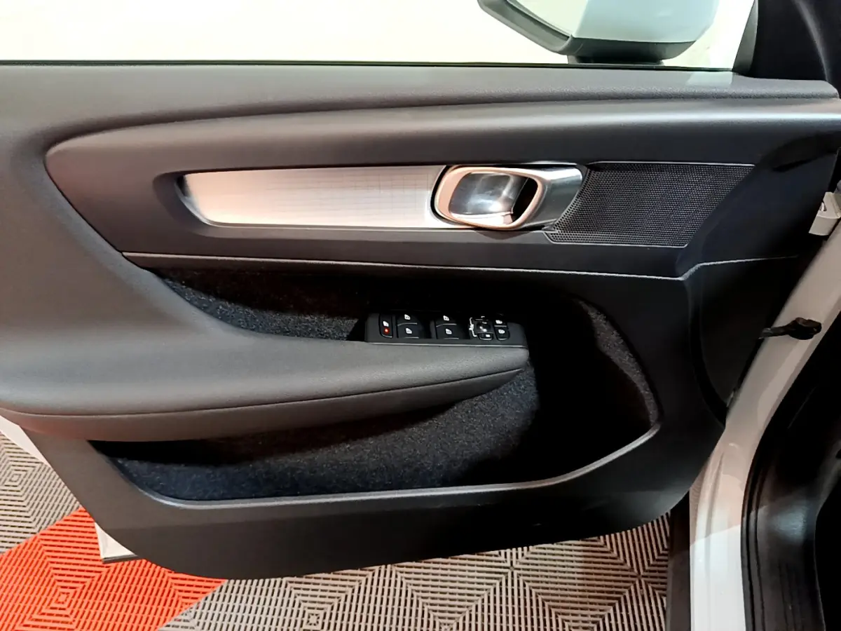 Gros plan sur la porte avant gauche intérieure du Volvo XC40 gris clair, avec poignée argentée et commandes électriques.