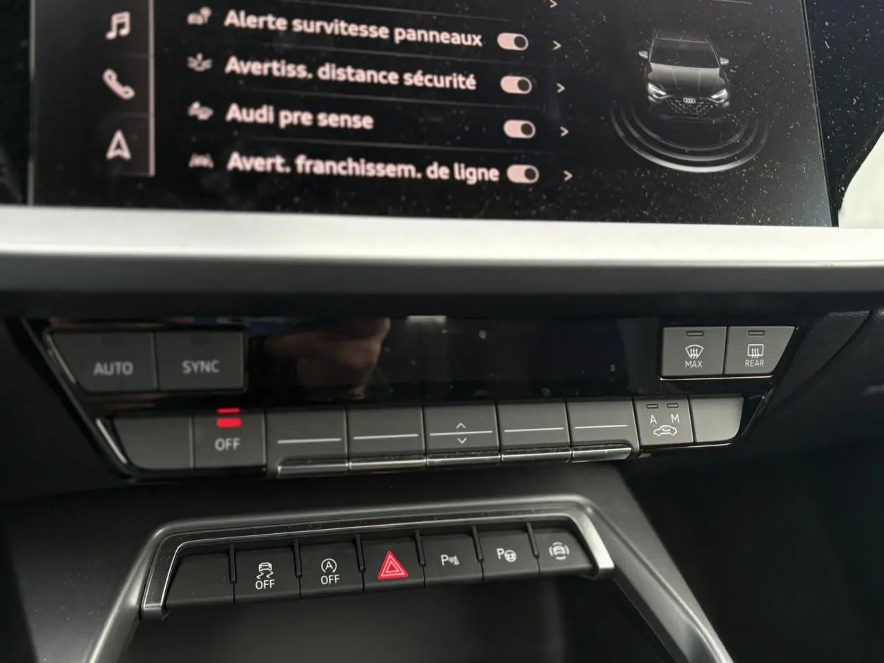 Vue rapprochée du tableau de bord de l'Audi A3 Berline 30 TFSI blanc, montrant les commandes climatisation et assistances.