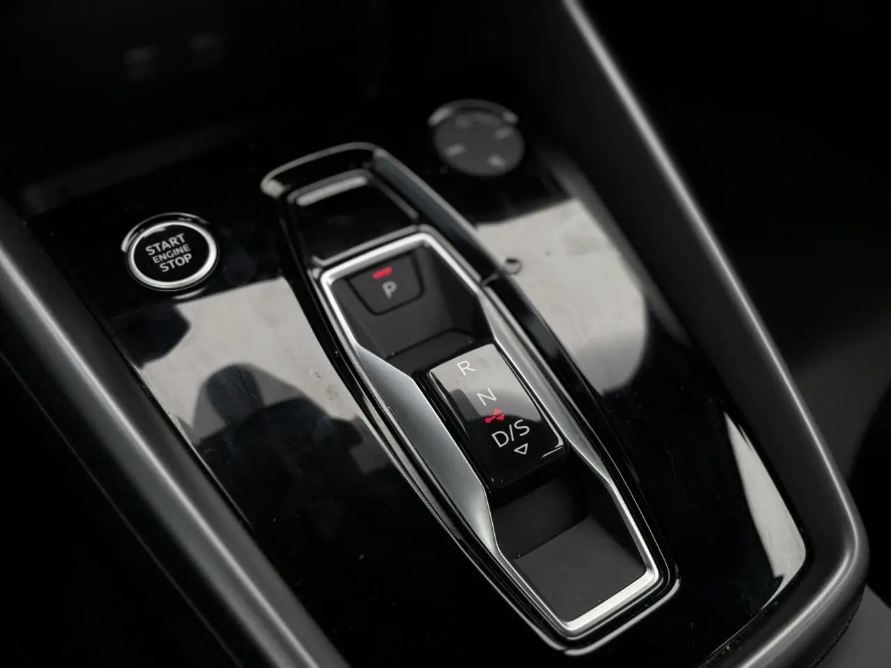 Gros plan sur la console centrale noire brillante avec levier de vitesses automatique et bouton Start/Stop d'une Audi A3 Berline.