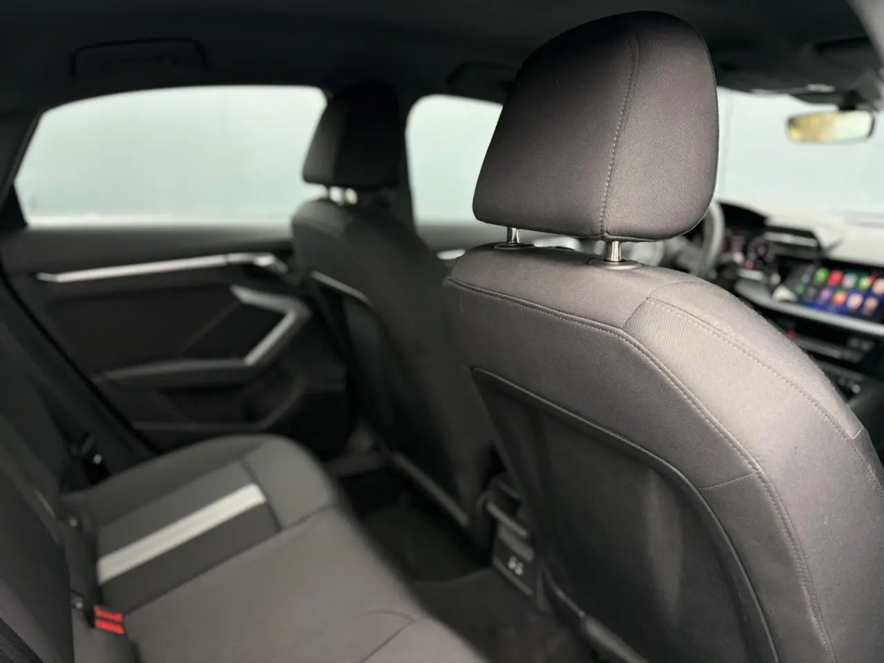 Vue intérieure arrière de l'Audi A3 Berline 2024 avec sièges tissu gris foncé et bande centrale claire.
