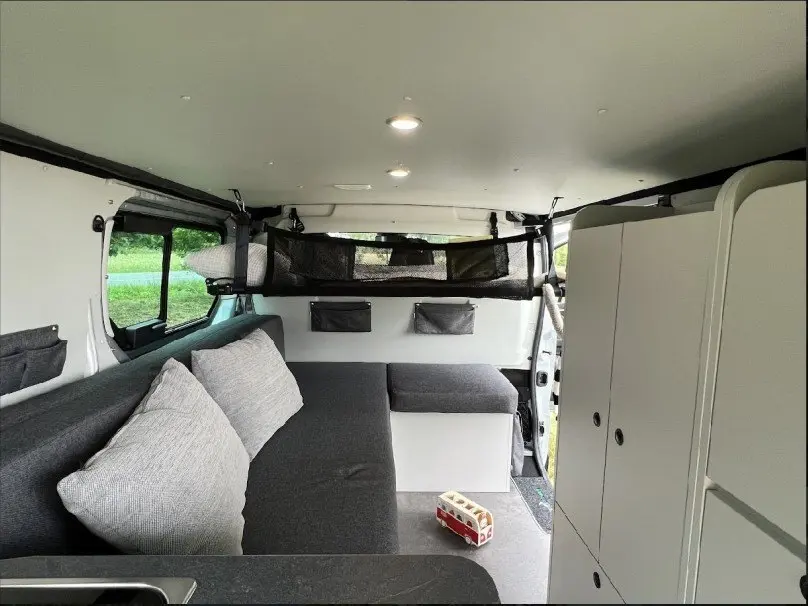 Intérieur du Renault Trafic Fourgon aménagé, vue latérale droite sur banquette grise et rangements blancs.