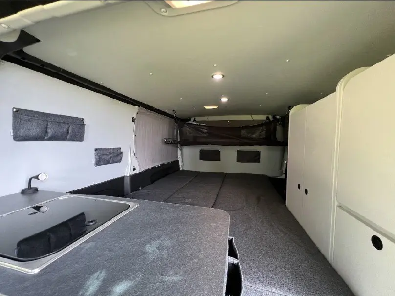 Intérieur aménagé du Renault Trafic Fourgon gris, vue de l'arrière vers l'avant avec espace couchage et rangements.