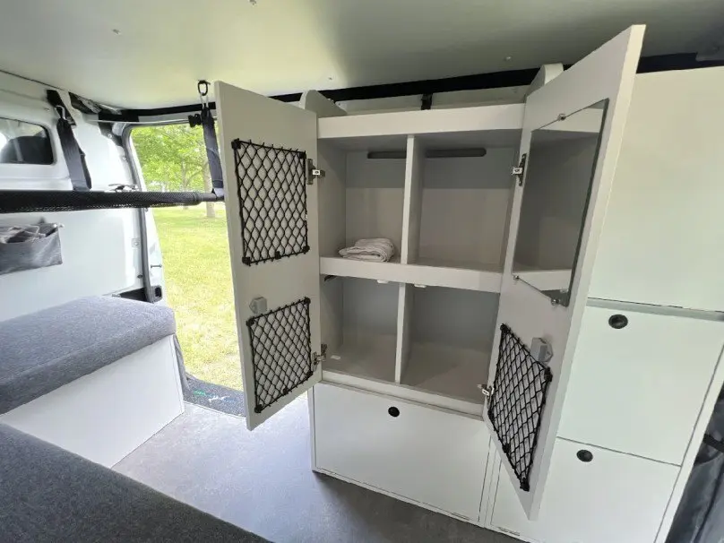 Intérieur du Renault Trafic Fourgon gris 2025, vue sur placard de rangement blanc ouvert avec filet noir, aménagement van.