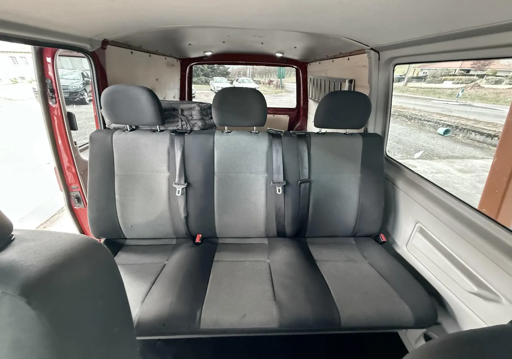 Banquette arrière noire vue de l'intérieur du Volkswagen Transporter rouge, avec trois appuie-têtes et ceintures de sécurité.