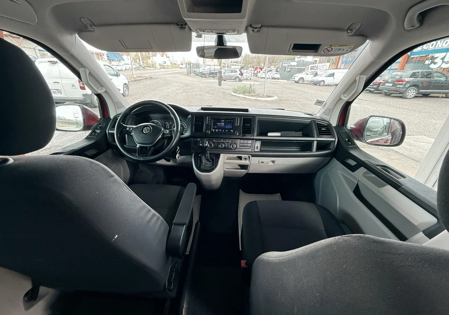 Vue intérieure avant du Volkswagen Transporter rouge, montrant le tableau de bord et les sièges en tissu noir.