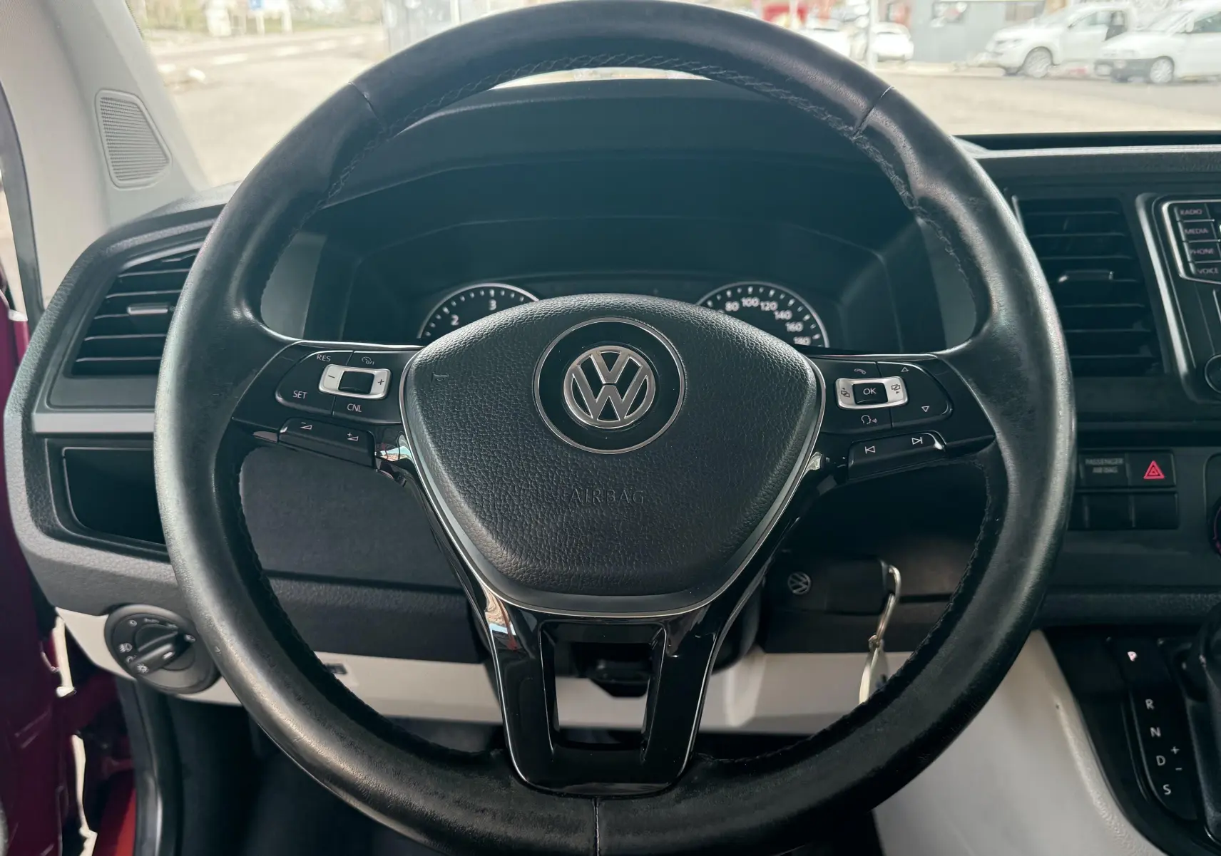 Vue rapprochée du volant noir de Volkswagen Transporter rouge, avec commandes intégrées et tableau de bord visible.