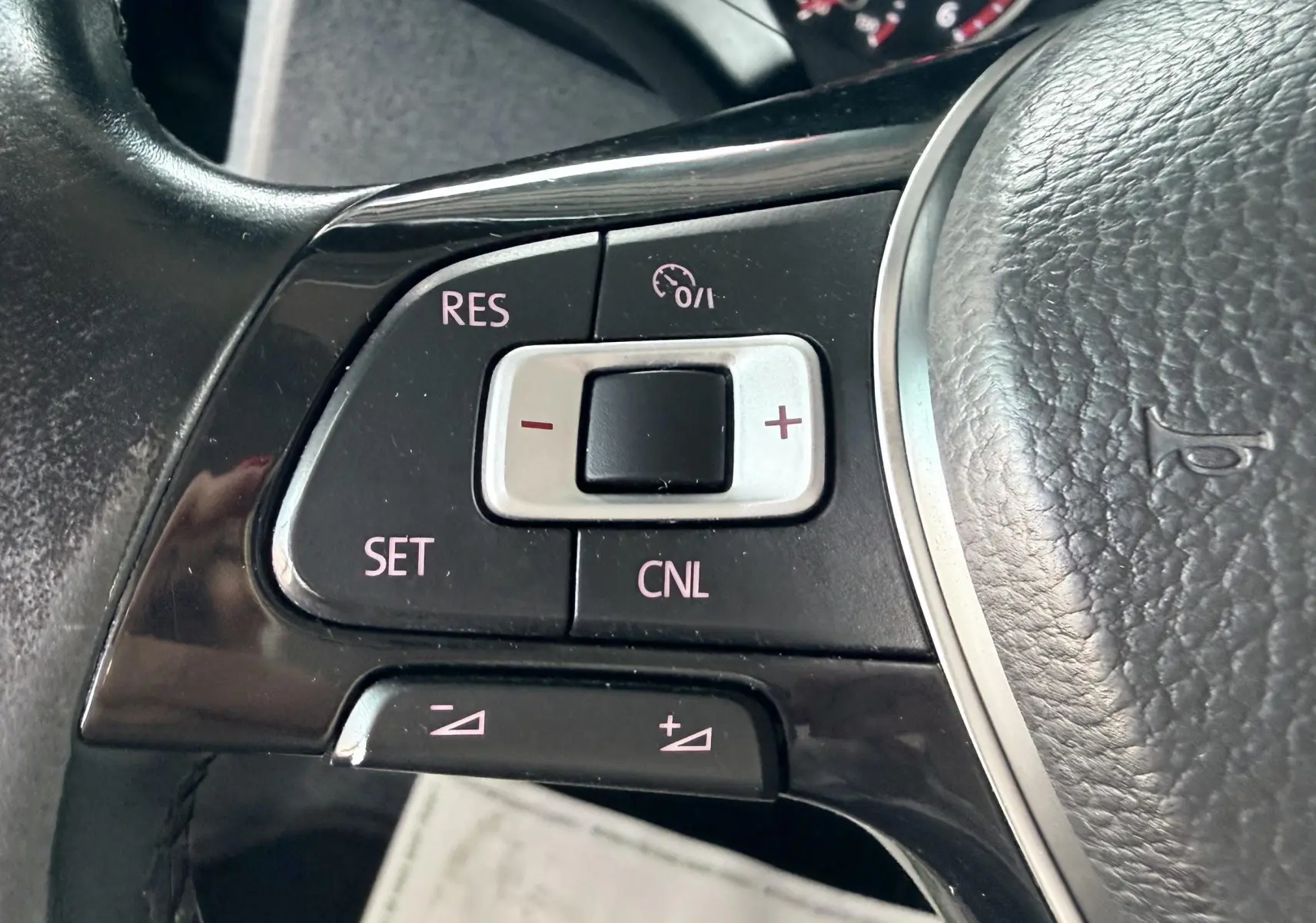 Gros plan sur les commandes du régulateur de vitesse sur le volant en cuir noir du Volkswagen Transporter rouge.