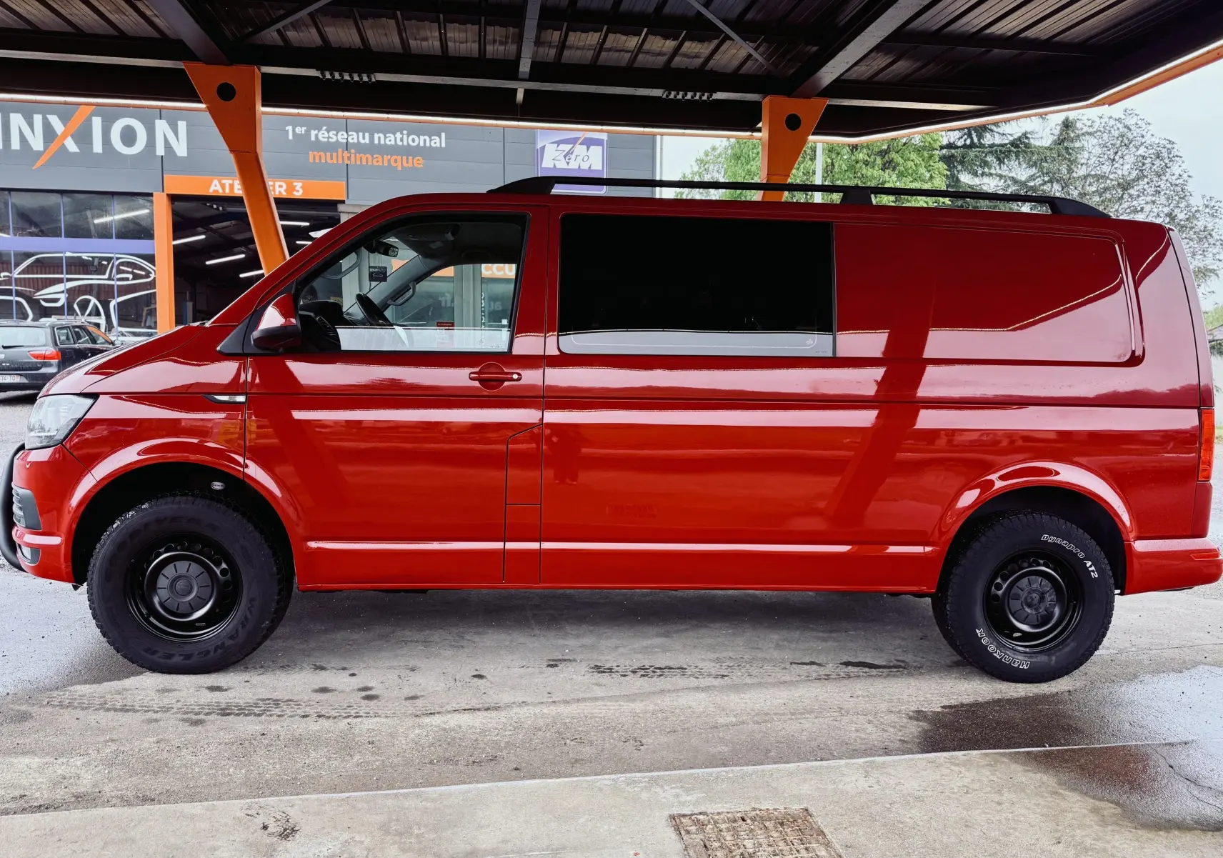 Vue de profil côté gauche du Volkswagen Transporter double cabine rouge, avec roues noires sous abri.