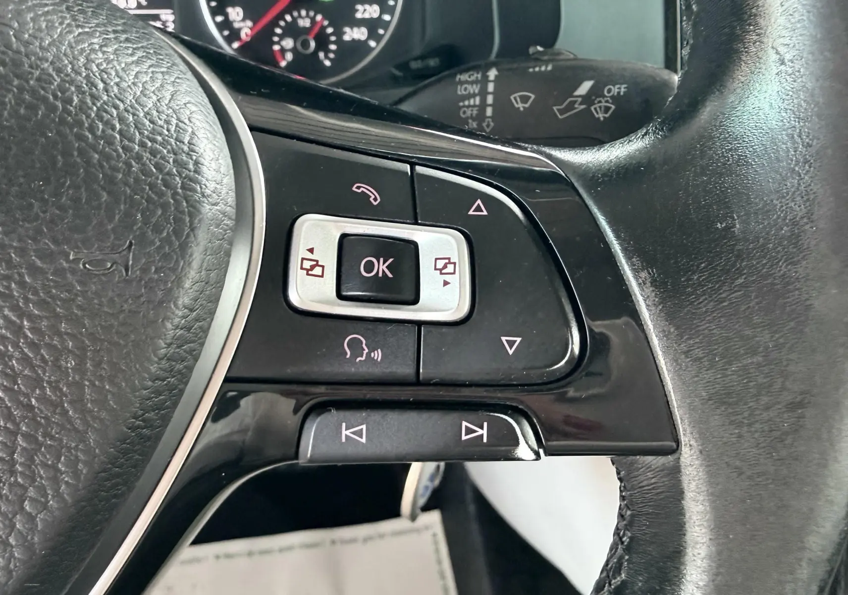 Gros plan sur les commandes multifonctions à droite du volant noir du Volkswagen Transporter rouge, avec cadrans du tableau de bord en arrière-plan.