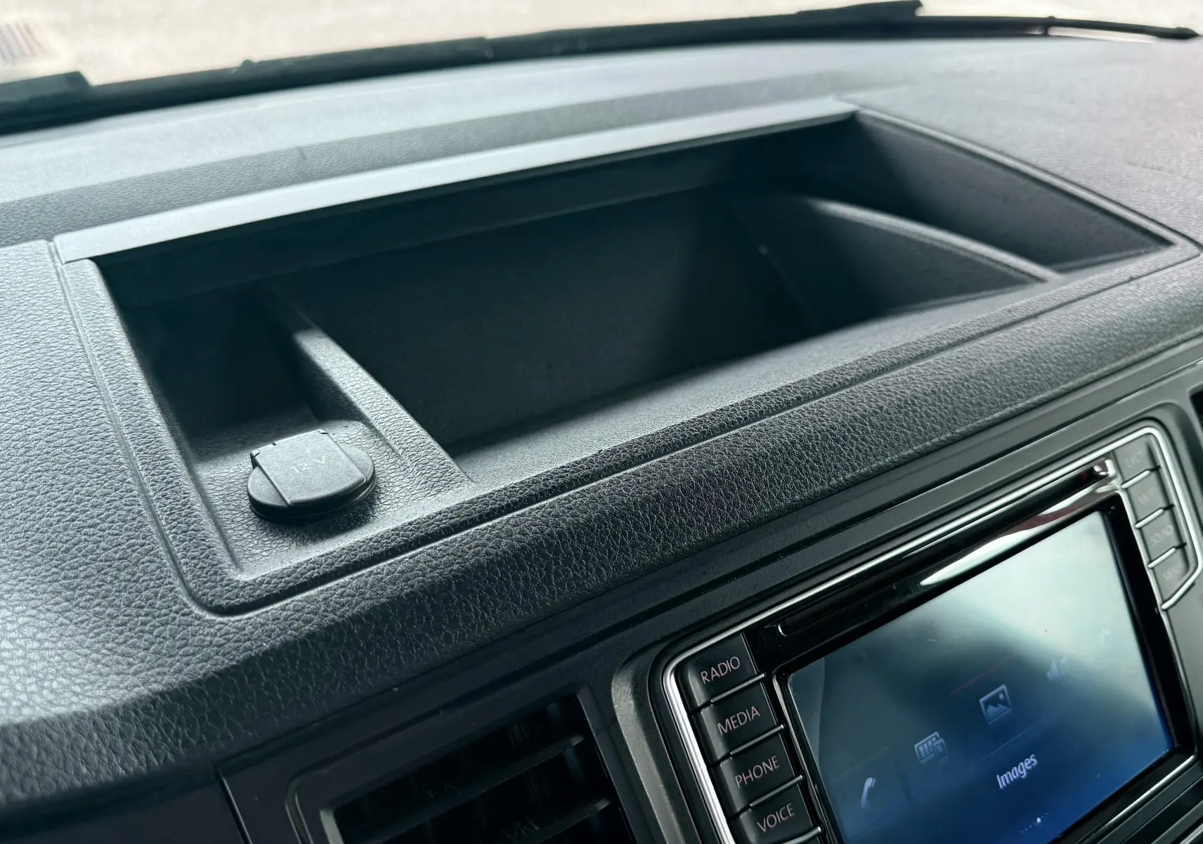 Vue rapprochée de la console centrale noire avec rangement et prise 12V du Volkswagen Transporter rouge.