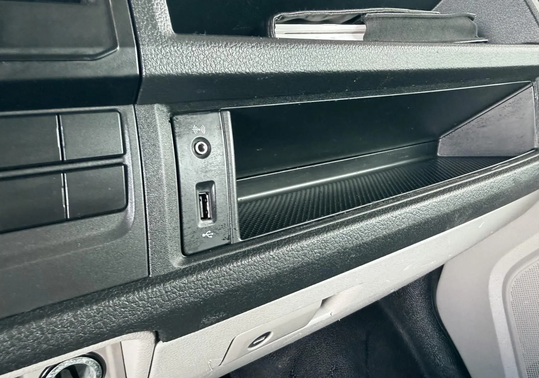 Détail de la console centrale noire avec prise USB et rangement du Volkswagen Transporter rouge, vue intérieure côté passager.