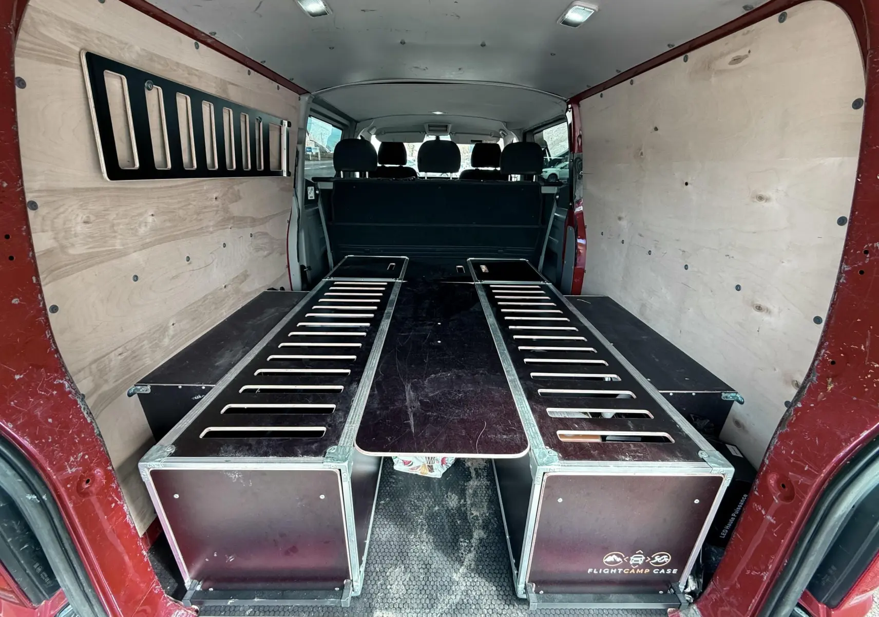 Vue arrière du Volkswagen Transporter rouge, aménagement intérieur avec caissons en bois et panneaux latéraux clairs.