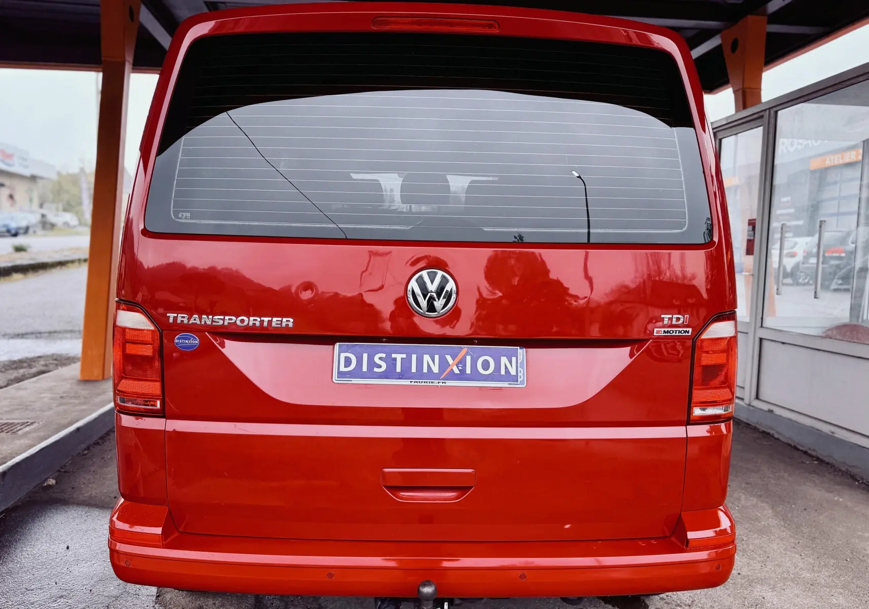 Vue arrière d’un Volkswagen Transporter rouge, version TDI 4Motion, avec logo et plaques visibles sous abri.