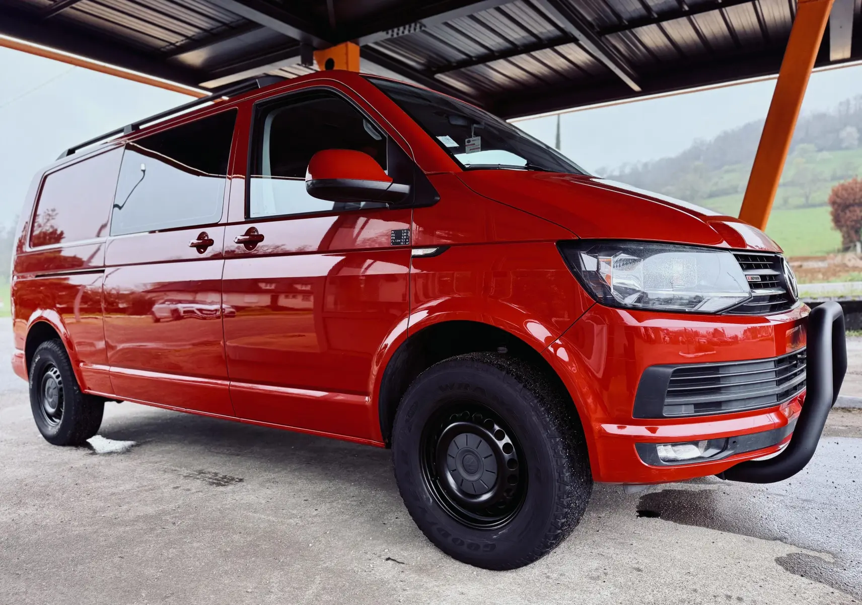 Vue 3/4 avant droite d'un Volkswagen Transporter rouge 2017 avec pare-buffle noir et jantes acier noires.