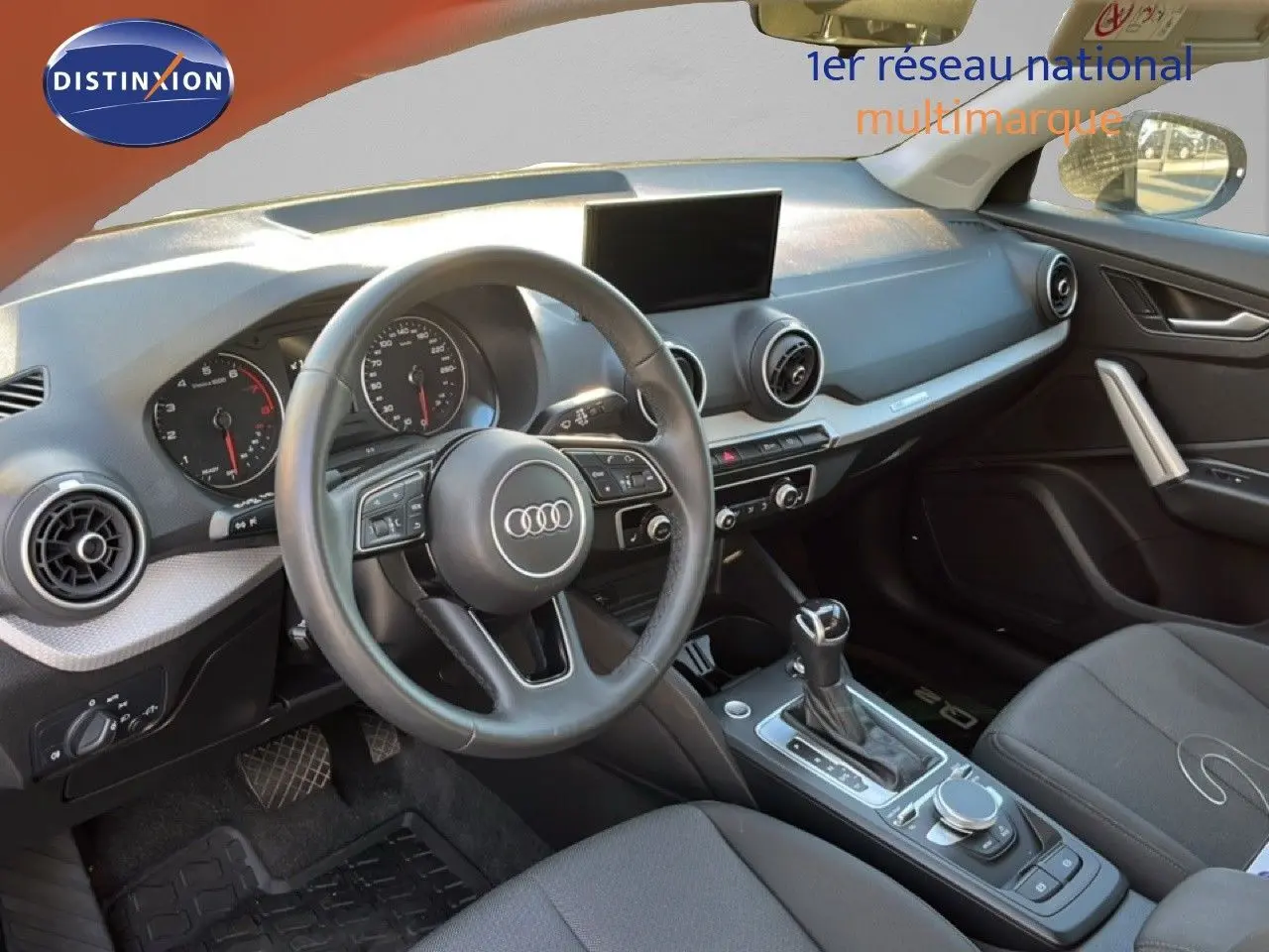 Intérieur de l'Audi Q2 35 TFSI 2023 vu côté conducteur, tableau de bord moderne avec volant multifonction et console centrale.