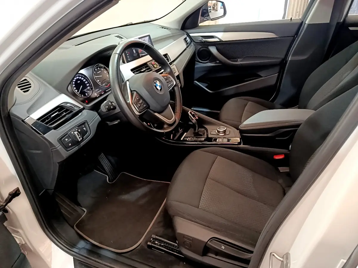 Vue intérieure côté conducteur du BMW X2 blanc 2023, avec tableau de bord moderne et sièges noirs en tissu.