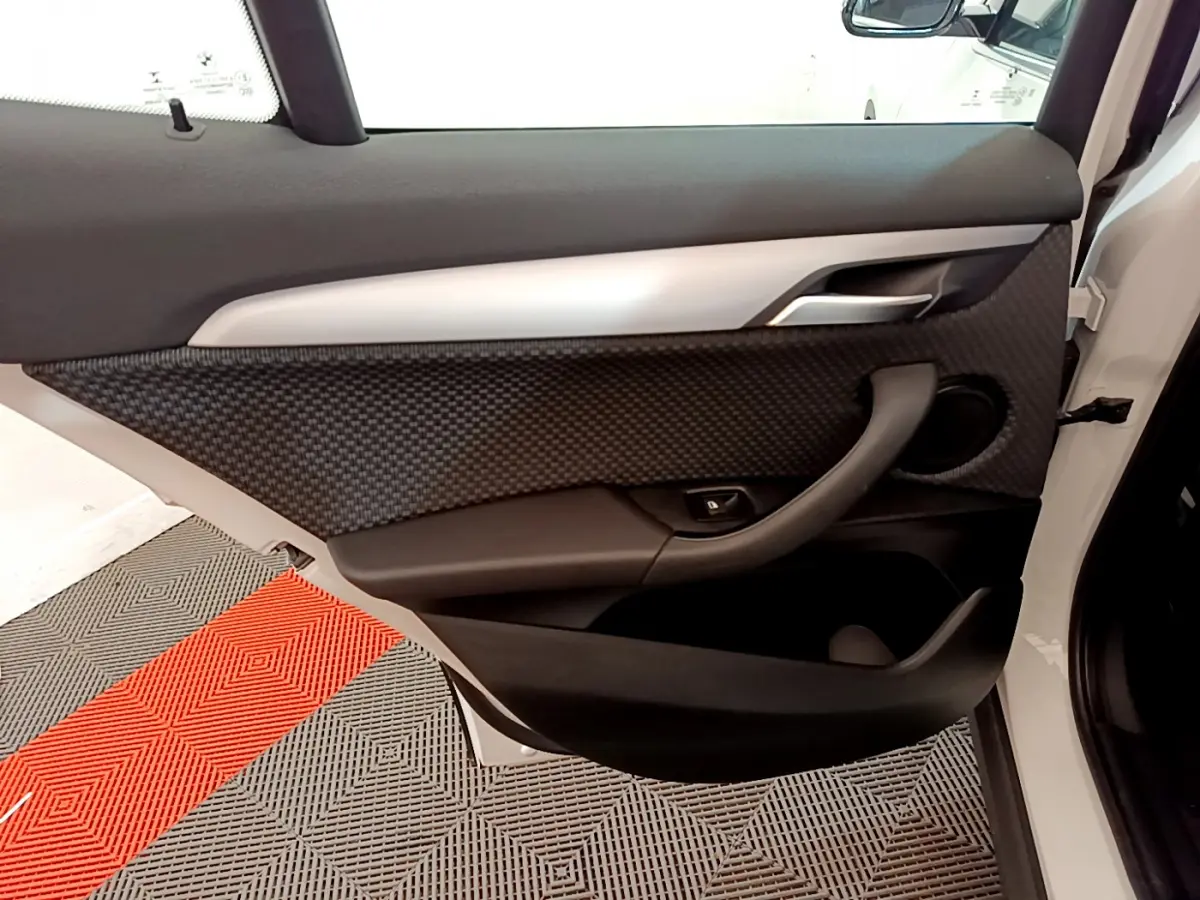 Intérieur de la porte côté gauche d'une BMW X2 blanche 2023 avec habillage noir texturé et poignée intégrée.