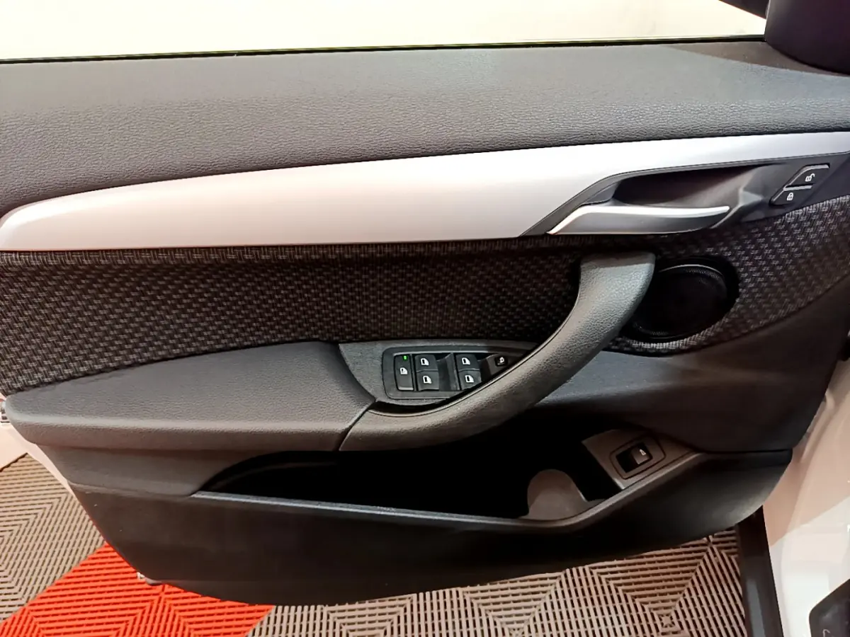 Vue rapprochée de la porte côté gauche d’une BMW X2 blanche, avec commandes électriques et garniture noire texturée.