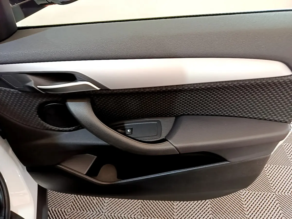 Détail de la porte côté gauche intérieure du BMW X2 blanc 2023 avec poignée noire et insert décoratif gris.