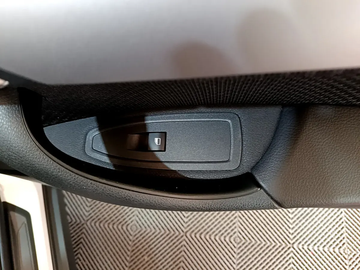 Bouton de commande de lève-vitre côté conducteur dans l'habitacle noir du BMW X2 blanc 2023.