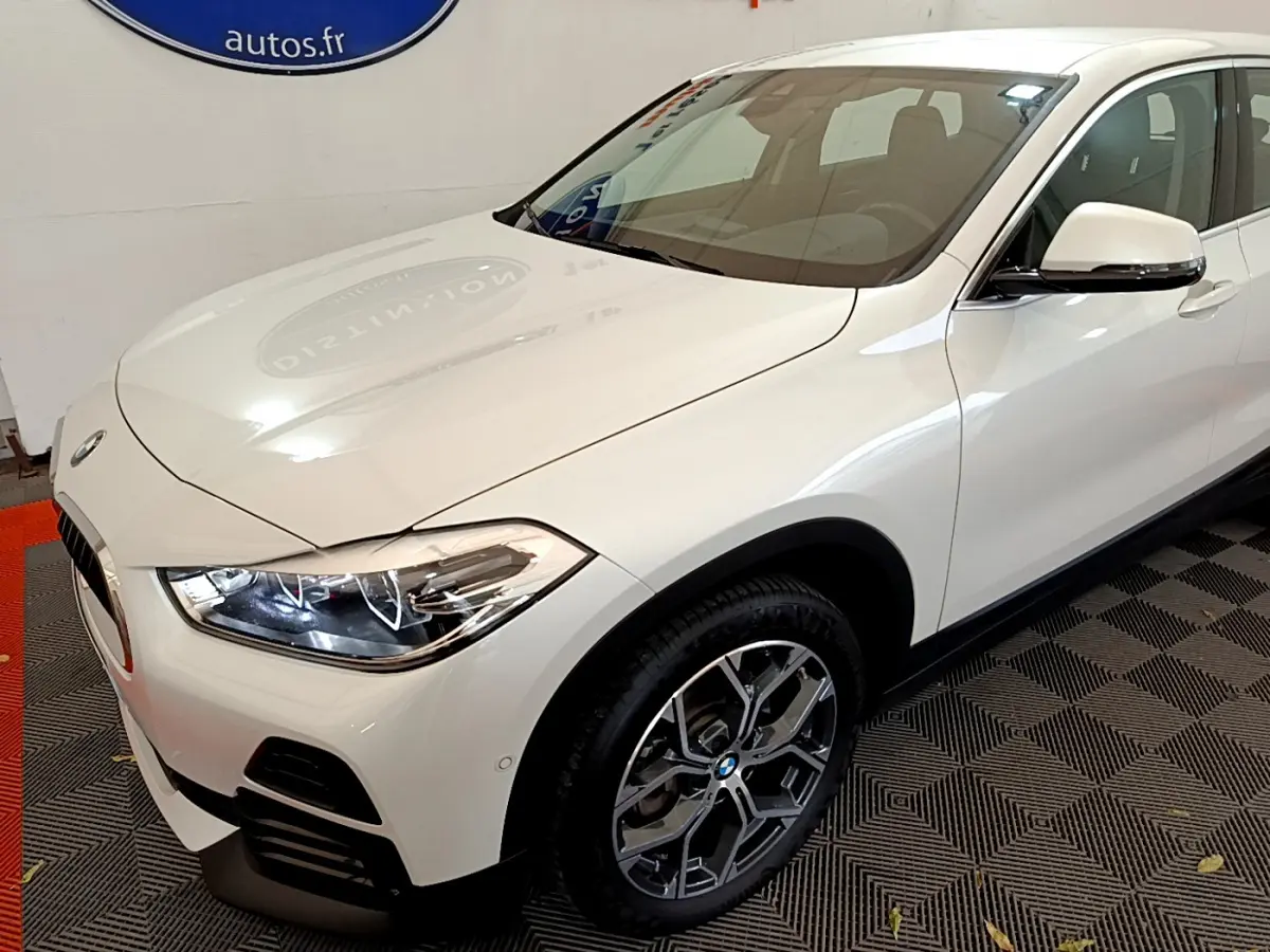 BMW X2 sDrive18i blanc en 3/4 avant droit, avec phares LED allumés et jantes alliage distinctives