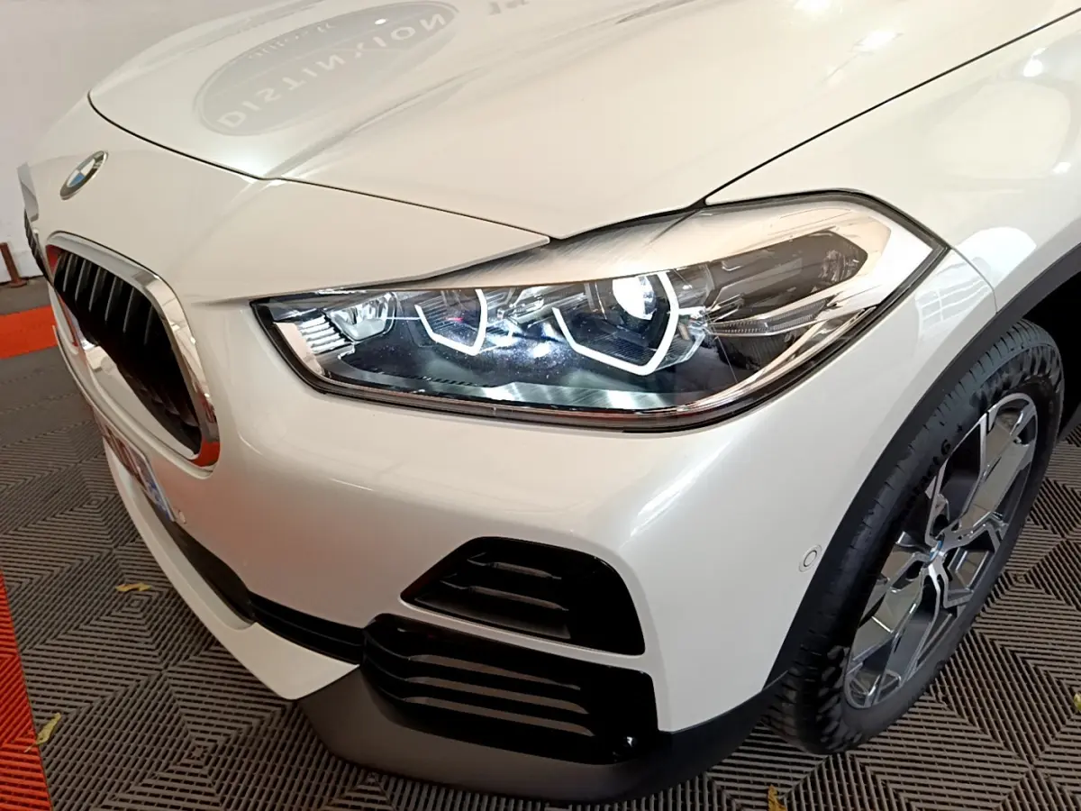 Gros plan sur l'avant droit blanc d'un BMW X2 2023, mettant en valeur le phare LED et la calandre caractéristique.