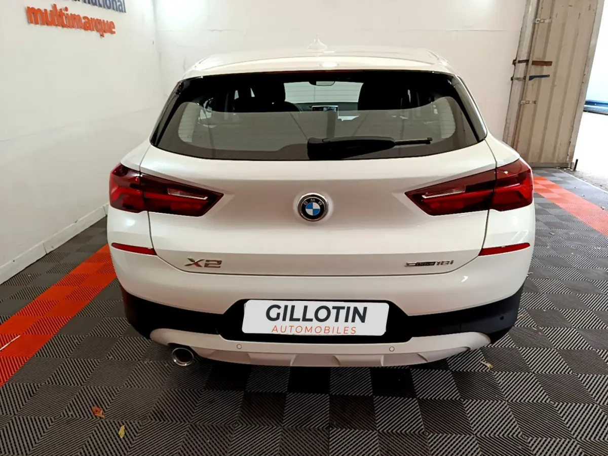 Vue arrière d'un BMW X2 blanc sDrive18i avec feux LED et sortie d'échappement visible en garage.