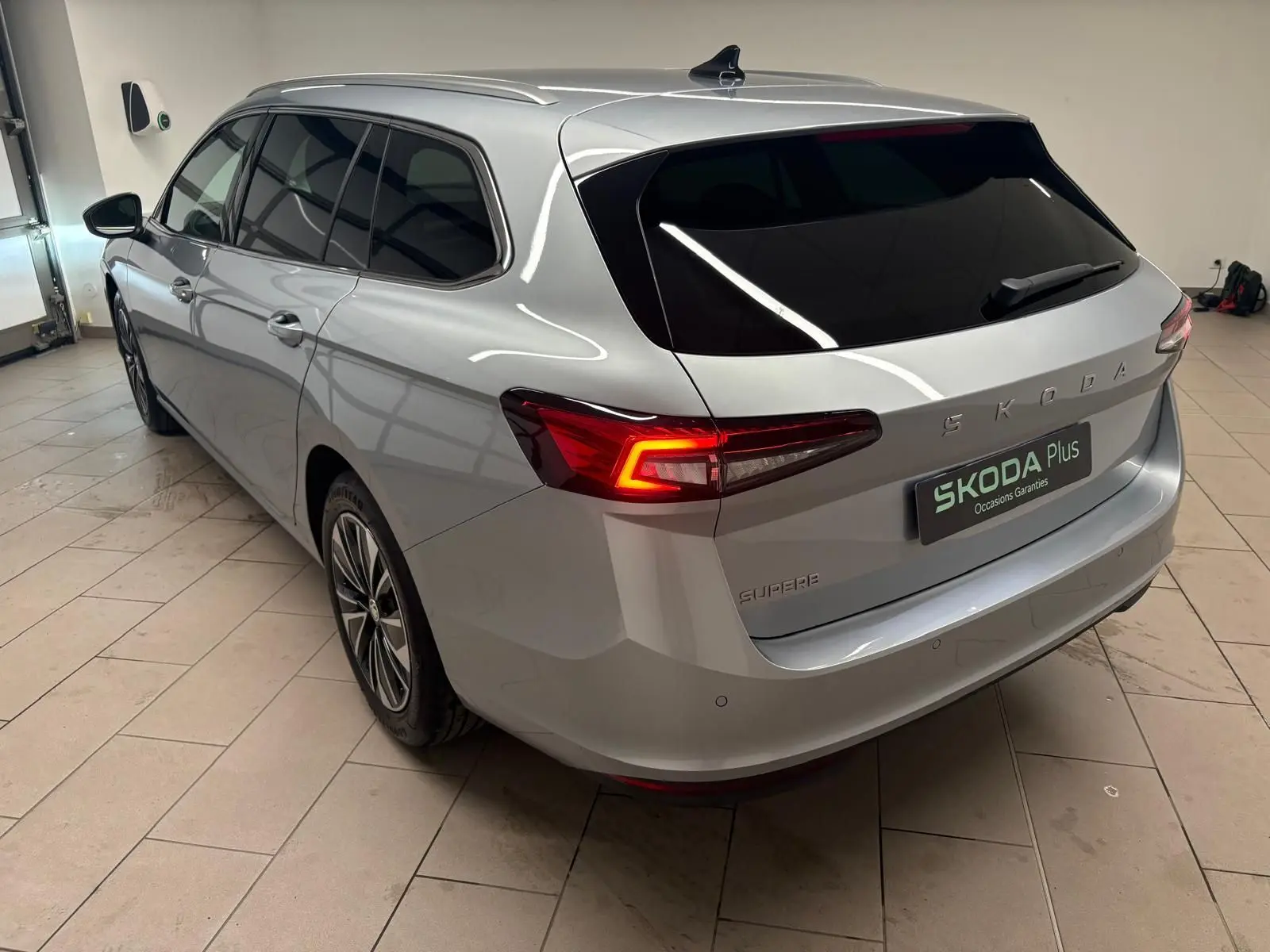 Vue 3/4 arrière droite d'une Skoda Superb Combi gris argent avec feux arrière allumés dans un garage.