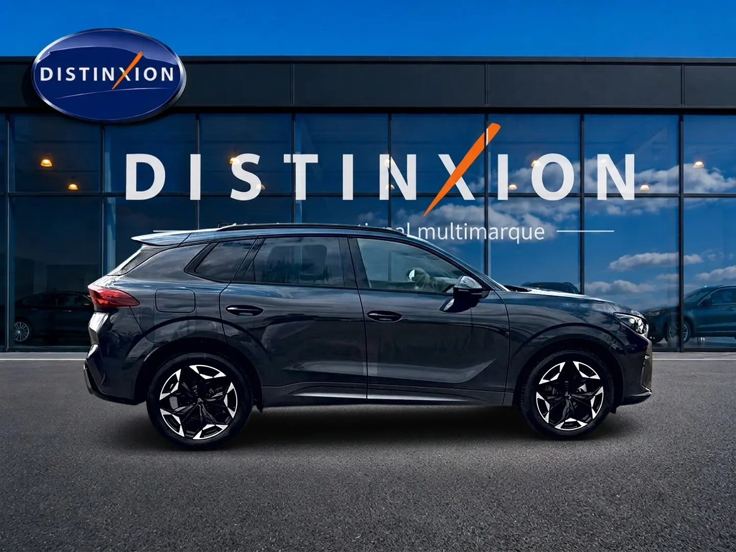 Vue latérale droite du SUV CUPRA Terramar gris Timanfaya avec jantes alu noires et toit noir, devant une vitrine Distinxion.