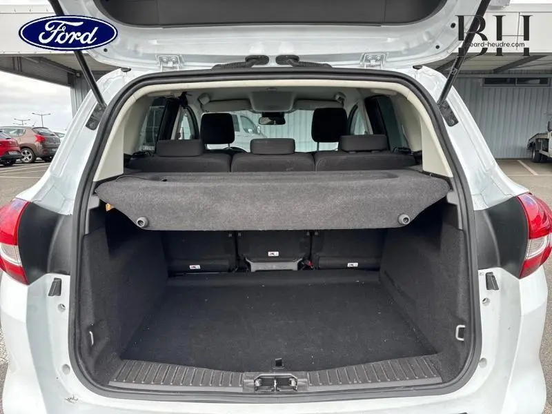 Coffre ouvert vu de l'arrière d'une Ford C-MAX blanc glacier, avec cache-bagages et sièges arrière en tissu noir.