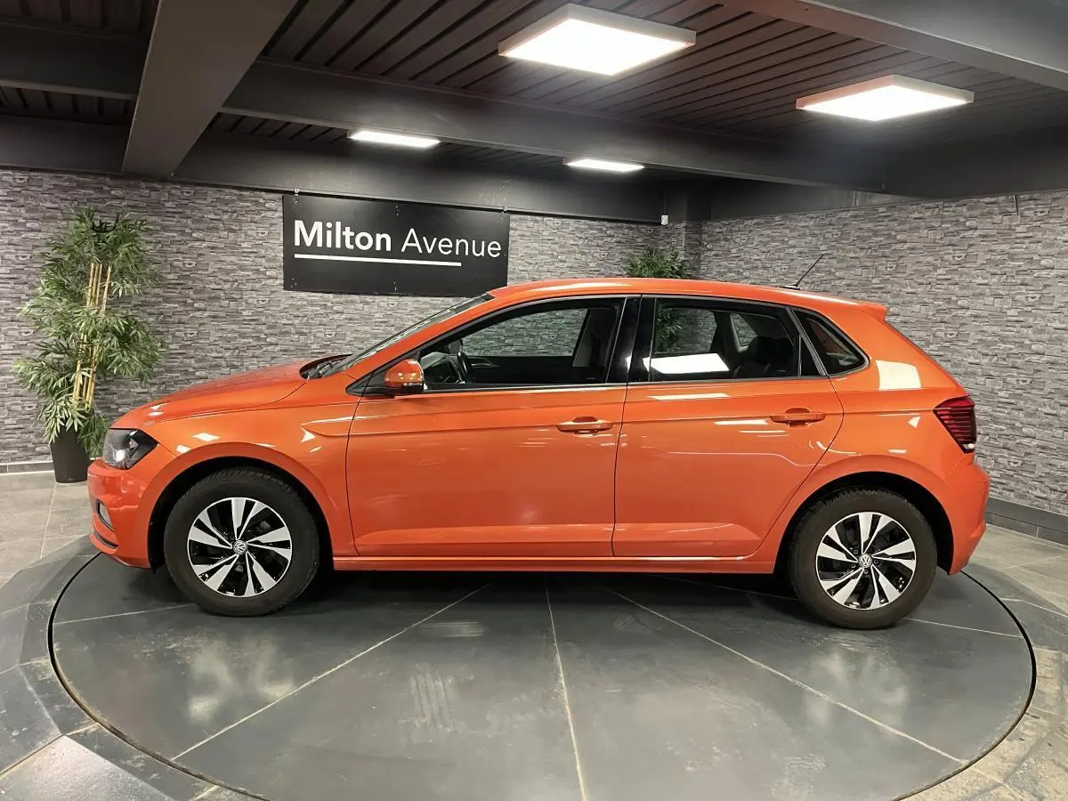 Volkswagen Polo orange vue de profil côté gauche, avec jantes alliage et intérieur visible en showroom.