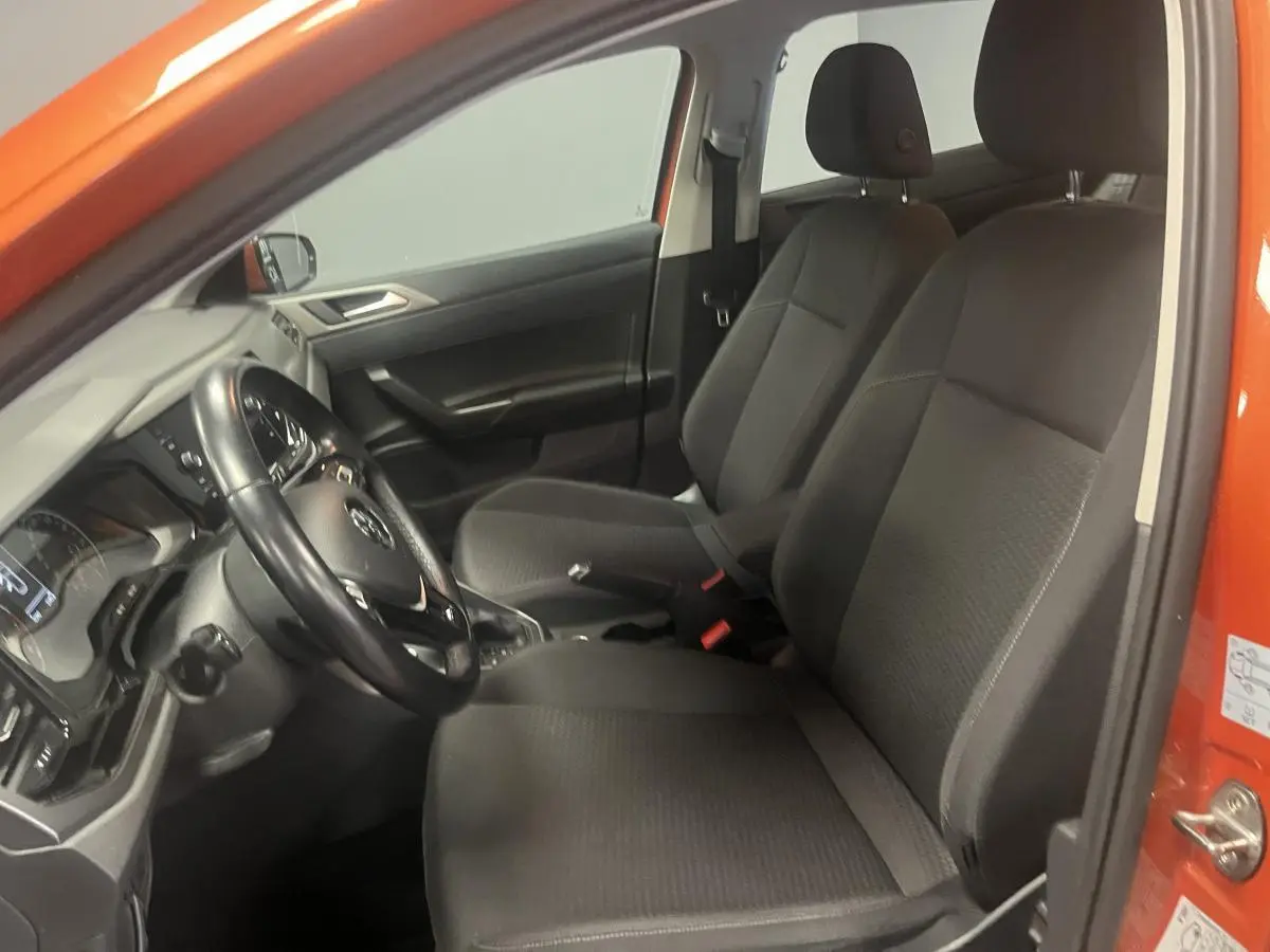 Intérieur côté conducteur d'une Volkswagen Polo orange 2019 avec sièges tissu noirs et volant cuir multifonction.