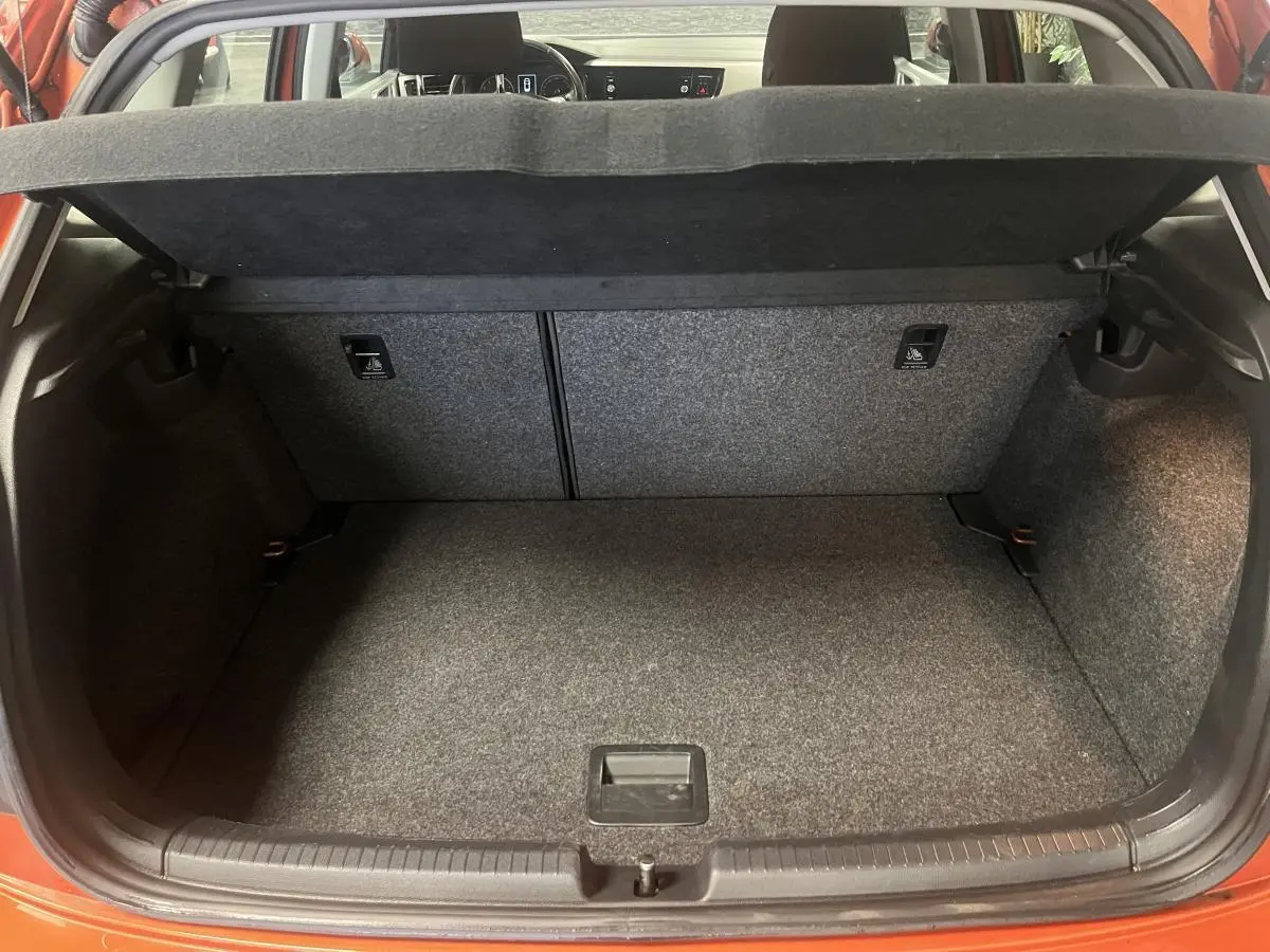 Coffre ouvert d'une Volkswagen Polo orange vue de l'arrière, montrant l'espace de chargement vide et la tablette cache-bagages.